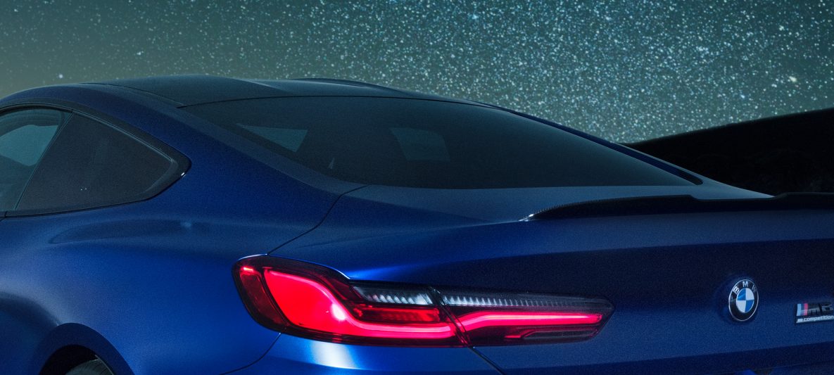 BMW M8 Competition Coupé in Marina Bay Blau metallic, nächtliche Nahaufnahme Schulterpartie mit M Heckspoiler aus Carbon.