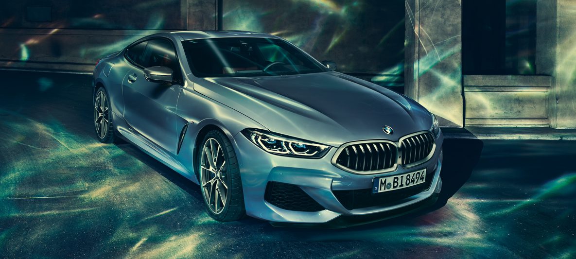 BMW M850i xDrive Coupé in Barcelona Blau metallic, Dreiviertel-Frontansicht links, stehend vor Gebäude.