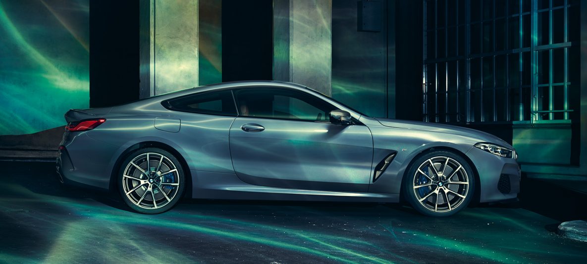 BMW M850i xDrive Coupé in Barcelona Blau metallic, Seitenansicht, stehend vor Gebäude.