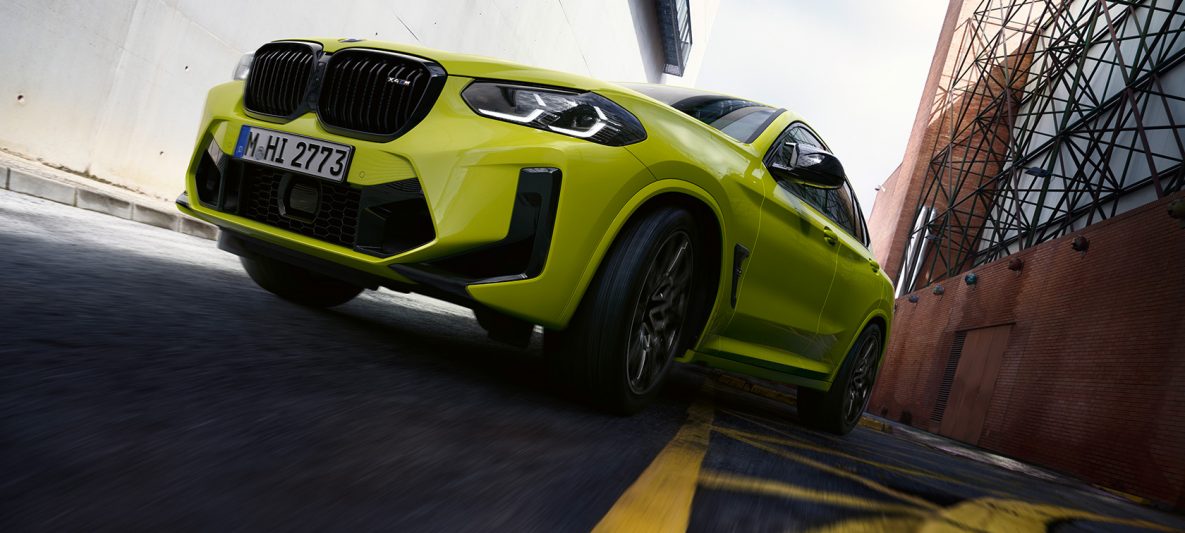 BMW X4 M Competition F98 LCI Facelift 2021 Sao Paulo Gelb Dreiviertel-Frontansicht mit Untersicht fahrend durch Häuserschlucht