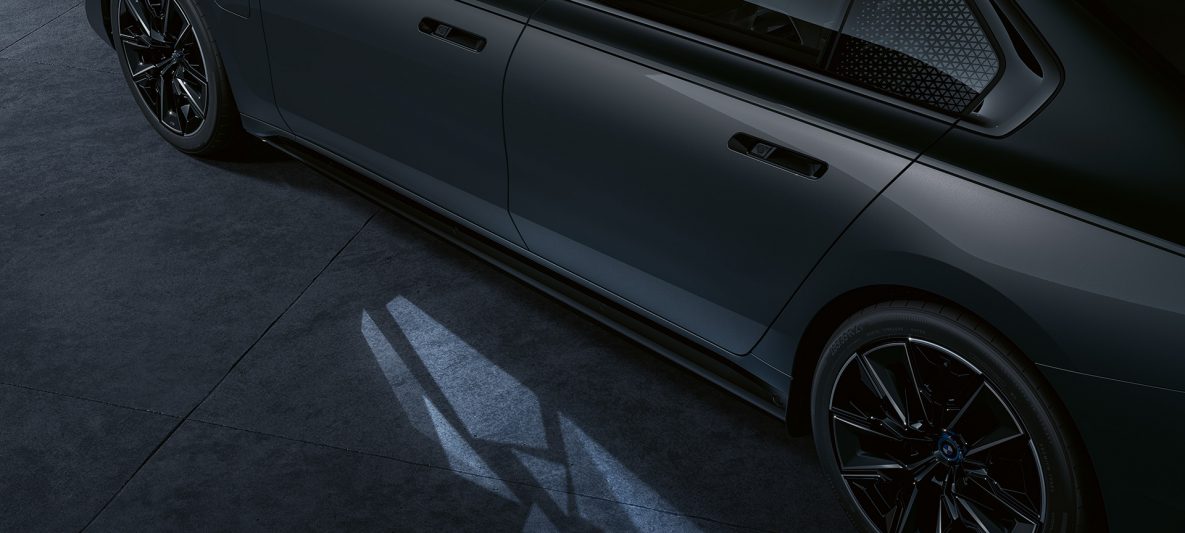 Lichtkonzept BMW M760e xDrive Limousine G70 Two-Tone Lackierung Saphirschwarz metallic BMW Individual Dravitgrau metallic Seitliche Nahaufnahme mit eingeschaltetem Welcome Light Carpet