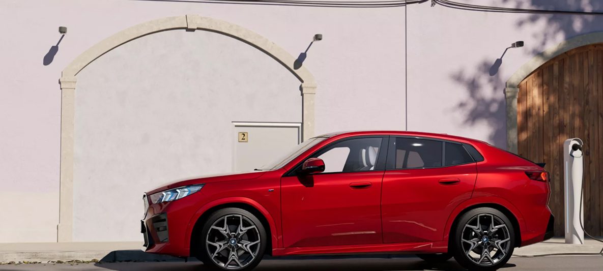 BMW iX2 in Dragonfire Red geparkt vor einem Landhaus bei sonnigem Wetter